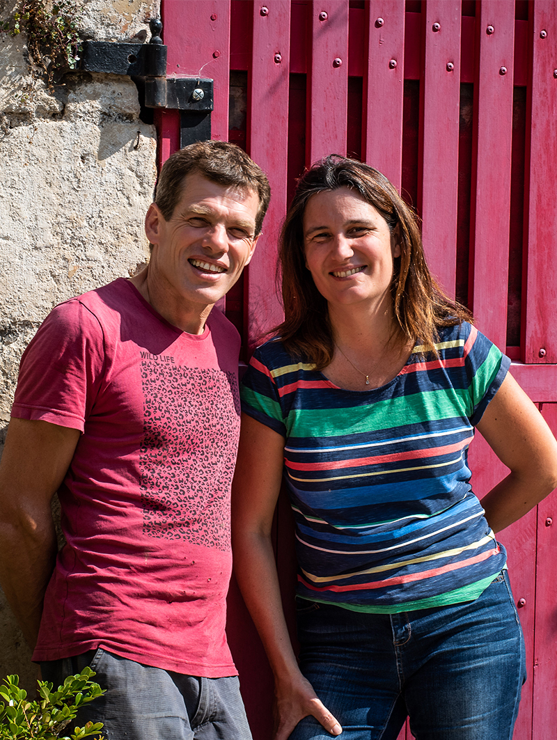 Domaine - Du vin aux liens- portrait vignerons un homme et une femme adossé à une porte en bois rouge